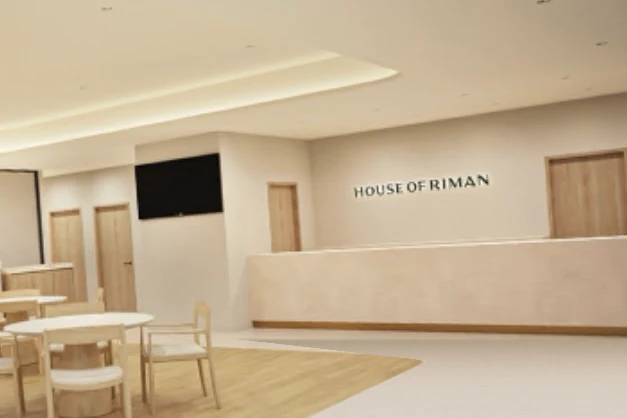 House of RIMANの内装の完成予想図。受付の壁に施設の名前、木の丸いテーブルと椅子
